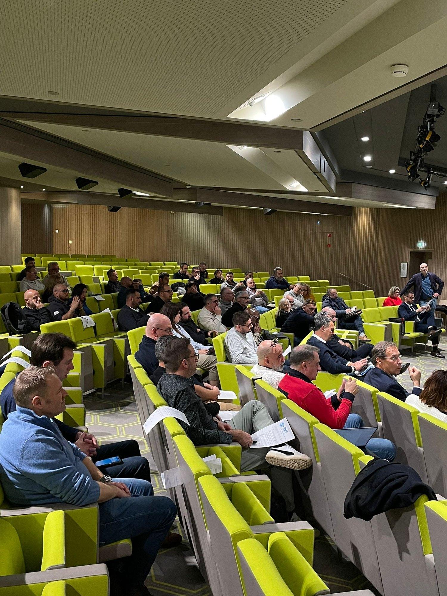 Vue d'ensemble d'un auditorium où une soixantaine d'adhérents de la FNMS suivent une présentation, documents en main.