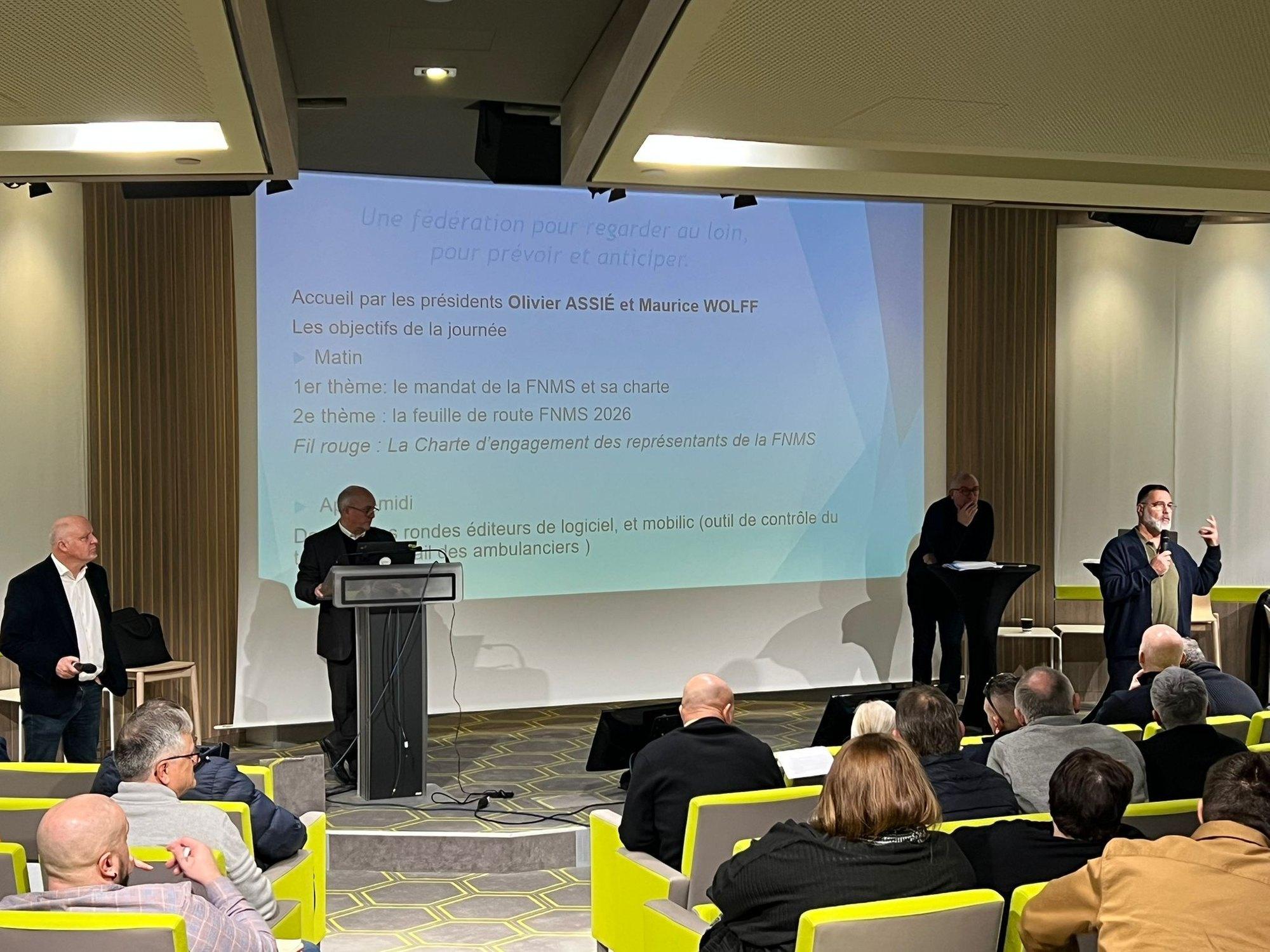 Ouverture d'une journée fédérale de la FNMS : deux intervenants au pupitre devant l'écran affichant le programme.